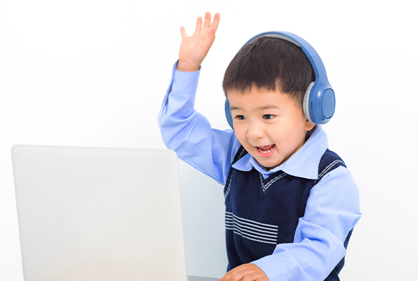 ヘッドホンをつけてパソコンに向かい、手を挙げて楽しそうに話す男の子