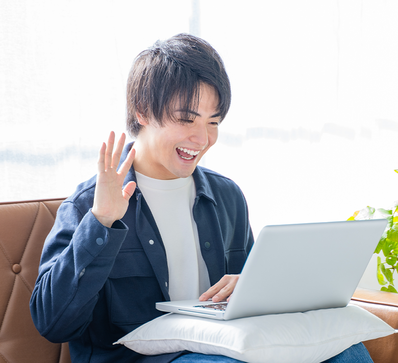 ノートパソコンに向かって手を振りながら英会話する若い男性