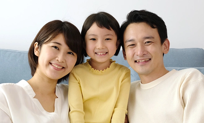 リビングでくつろいだ様子で笑顔を見せる、両親と幼い女の子の3人家族