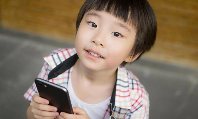 スマートフォンを両手で持ち、興味深そうな表情で上を見上げている男の子