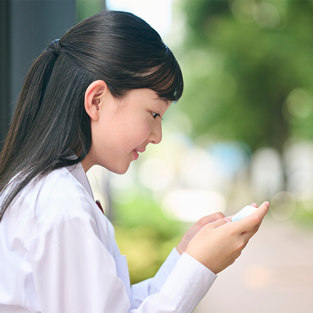 屋外でスマートフォンを見つめる女子学生