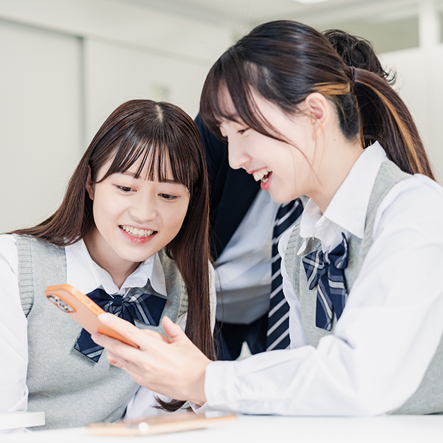 スマートフォンを見ながら笑顔で会話する女子高校生たち