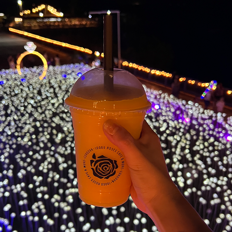 光るバラを背景に夜にコーヒーカップを持つ手