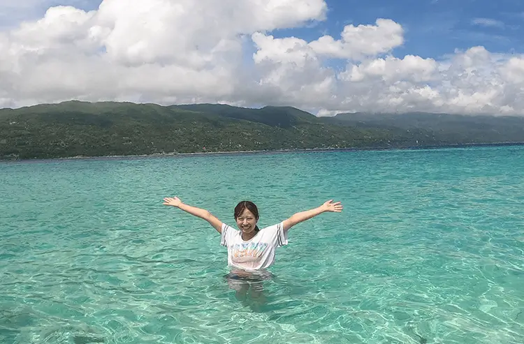 エメラルドグリーンの海で両手を広げる女性