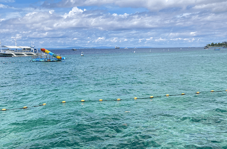 青い海にボートと浮き台が浮かび曇り空が広がる屋外の海の景色