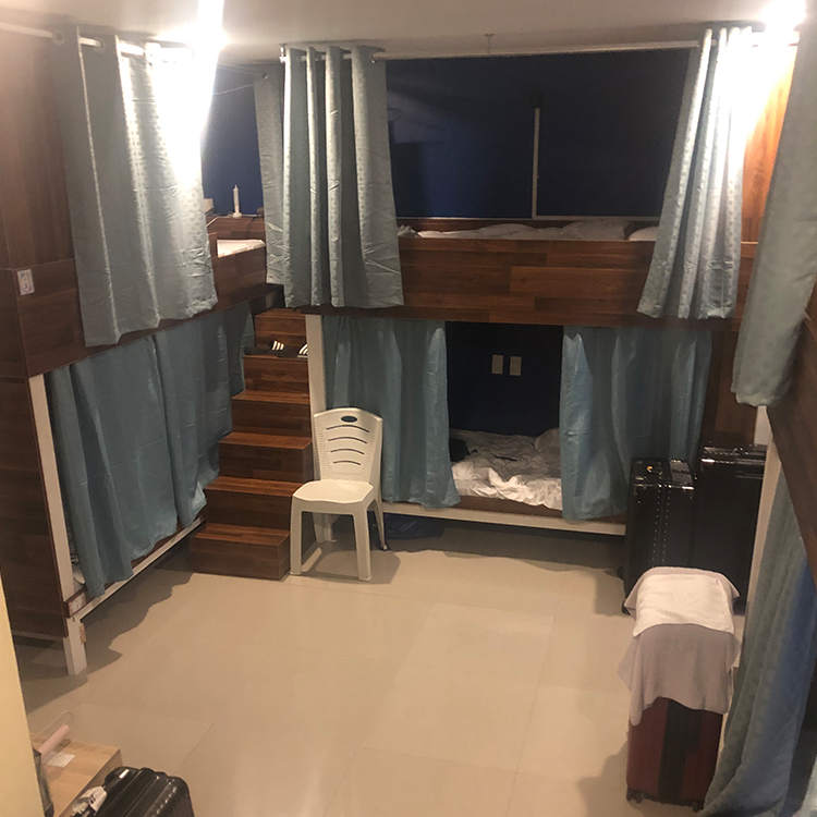 二段ベッドと青いカーテンがある屋内の宿泊施設、木製階段